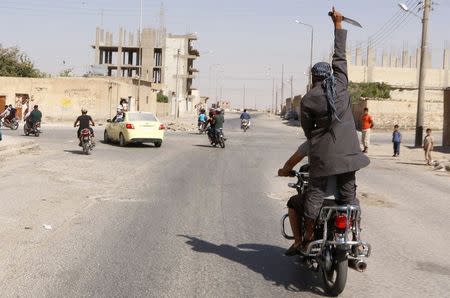 A man holds up a knife as he rides on the back of a motorcycle touring the streets of Tabqa city with others in celebration after Islamic State militants took over Tabqa air base, in nearby Raqqa city August 24, 2014. REUTERS/Stringer