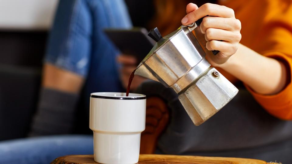 Midsection of young woman holding coffee maker while pouring coffee into cup.