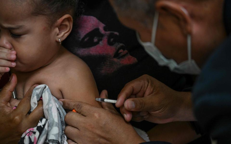 A girl accompanied by her mother receives a dose of measles and rubella vaccine from medical personnel at a community health center in the Lidice neighborhood in Caracas, - YURI CORTEZ/AFP via Getty Images