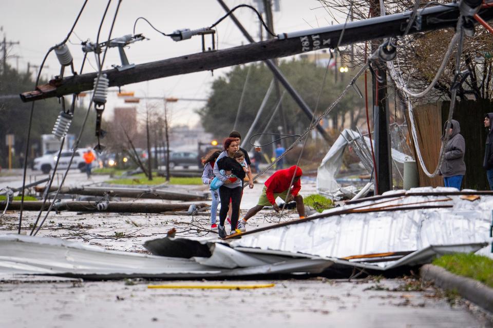 People cross under downed power lines where a tornado was reported to pass along Mickey Gilley Boulevard near Fairmont Parkway on Jan. 24, 2023, in Pasadena, Texas.