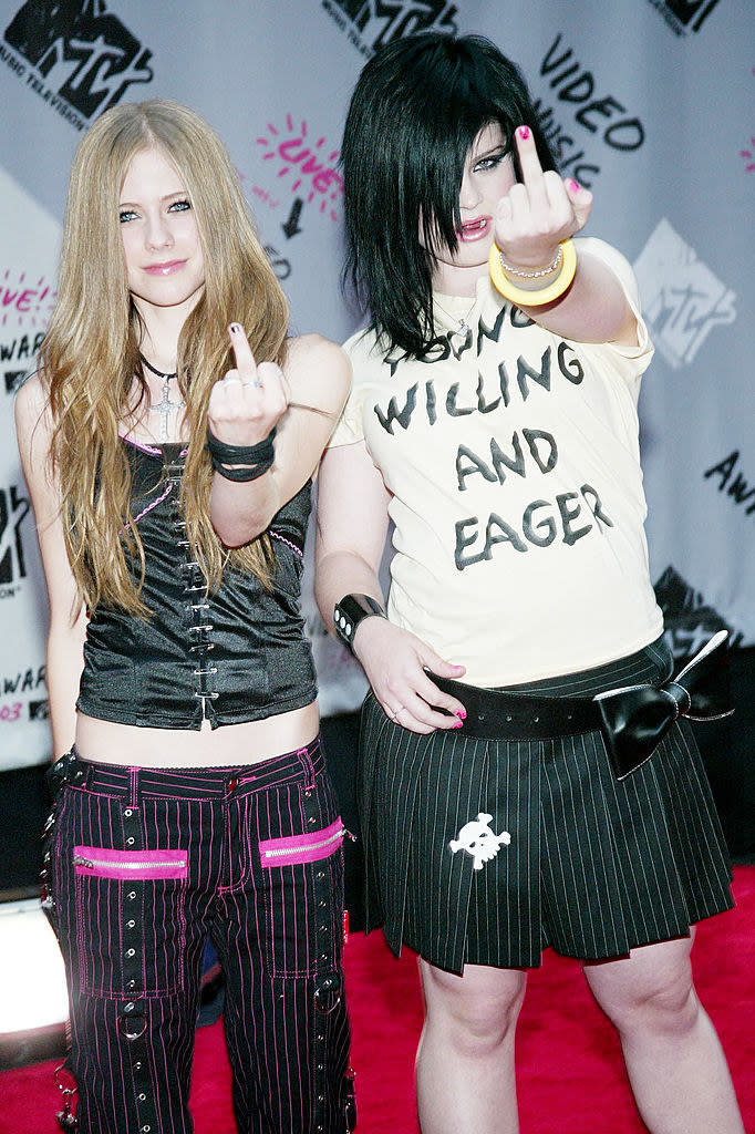 Avril Lavigne and Kelly Osbourne are giving the camera the finger on the red carpet; Kelly is wearing a "Young Willing and Eager" T-shirt