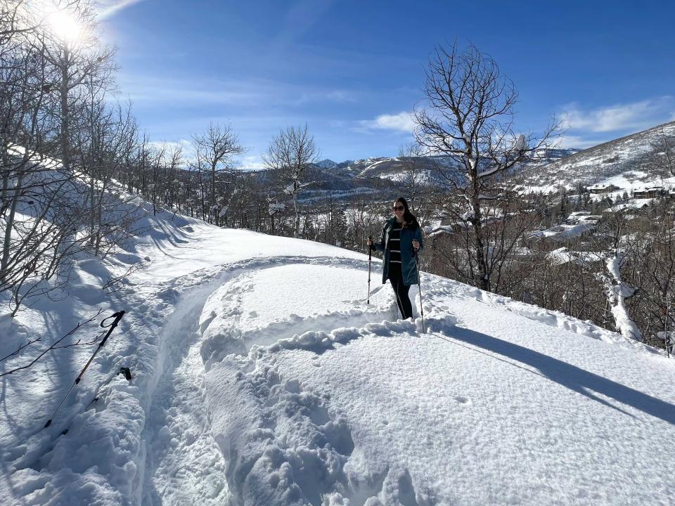 A woman on a snow trail in snowshoes with poles.