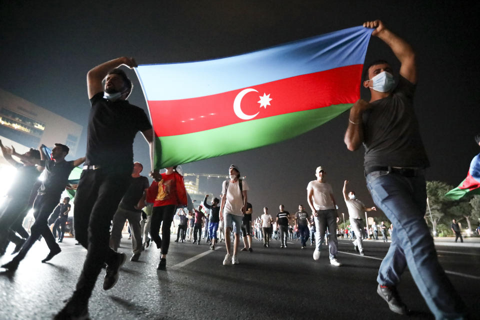 People carry an Azerbaijn's national flag as they rally in support of Azerbeijan's Army in Baku, Azerbaijan, Tuesday, July 14, 2020. Skirmishes on the volatile Armenia-Azerbaijan border escalated Tuesday, marking the most serious outbreak of hostilities between the neighbors since the fighting in 2016. (AP Photo/Aziz Karimov)