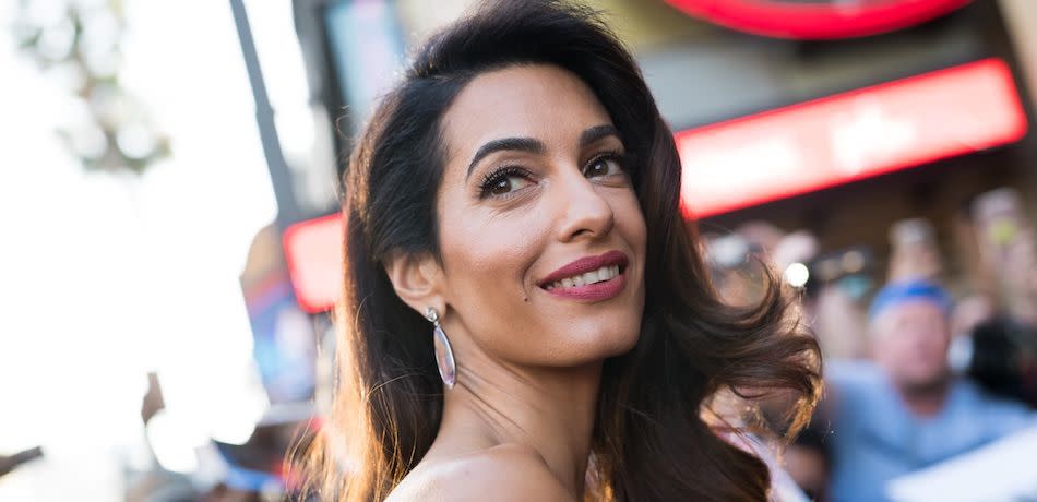 Amal Clooney looks over her shoulder and smiles at the red carpet.