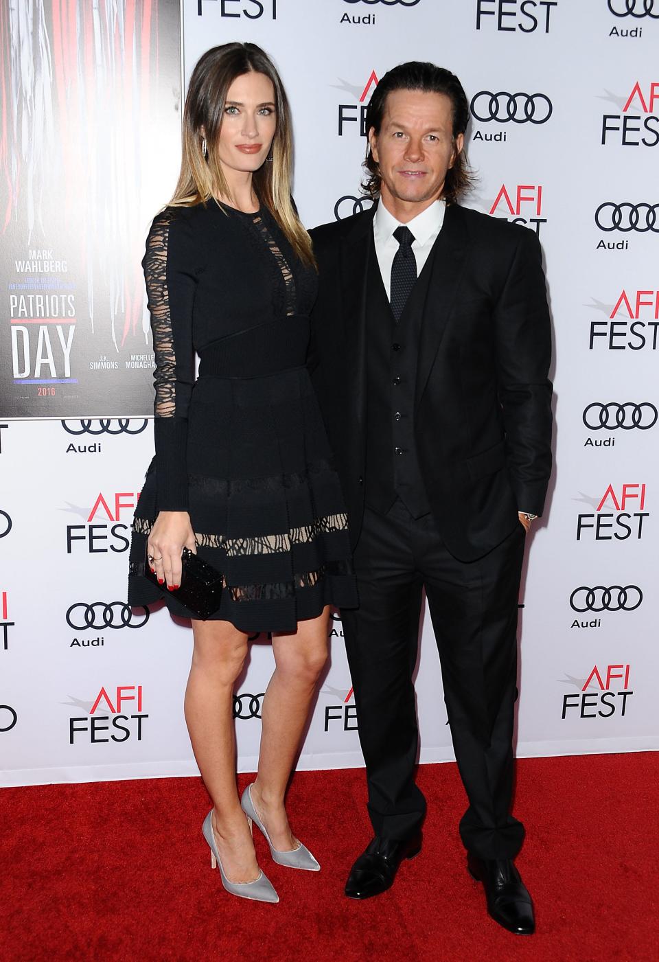 Rhea Durham in a black mini dress and heels standing taller than Mark Wahlberg in a black suit.