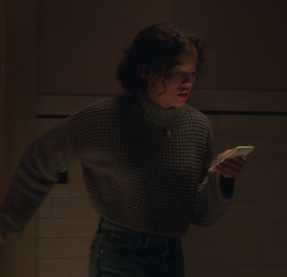 Zoya wears a dark cropped cowl neck sweater and high waisted jeans