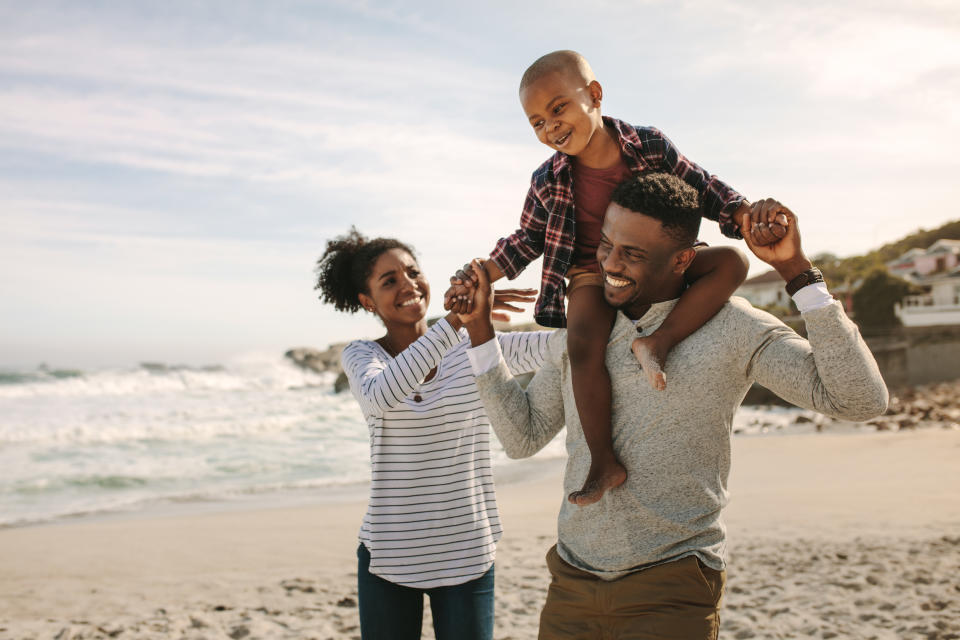 Parents carrying son on shoulders on beach vacation. African family of mother and father carrying son on his shoulders on vacation.