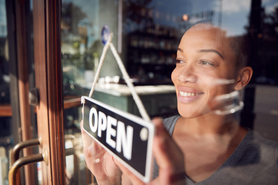 Female Owner Of Start Up Coffee Shop Or Restaurant Turning Round Open Sign On Door