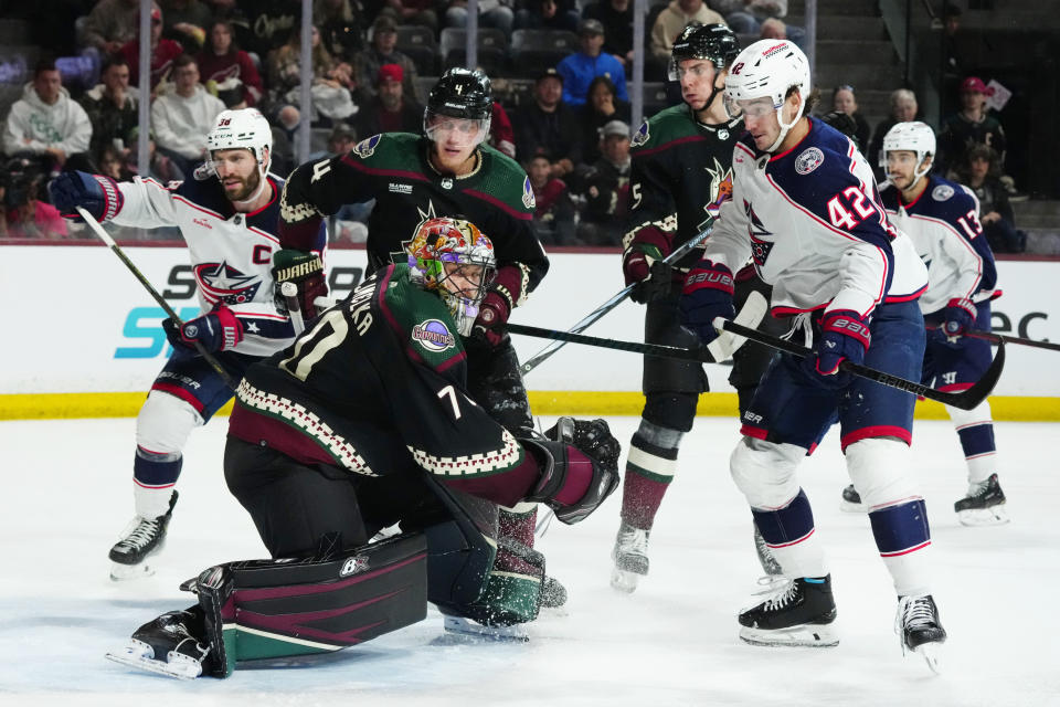 Arizona Coyotes goaltender Karel Vejmelka, left, makes a save on a shot by Columbus Blue Jackets center Alexandre Texier (42) as Blue Jackets center Boone Jenner (38), Coyotes defenseman Juuso Valimaki (4), Coyotes' Michael Kesselring (5) and Blue Jackets left wing Johnny Gaudreau (13) look on during the second period of an NHL hockey game Tuesday, March 26, 2024, in Tempe, Ariz. (AP Photo/Ross D. Franklin)