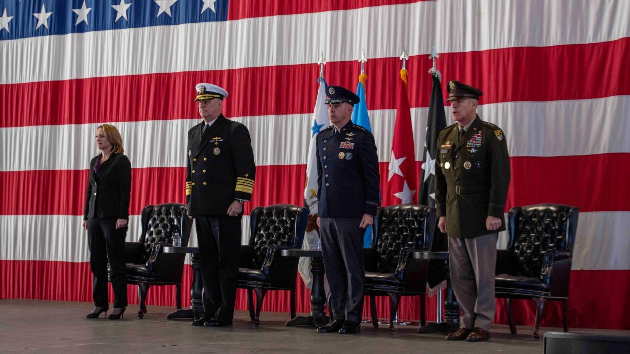  Four people, three of whom are in u.s. military uniforms, stand in front of an American flag. 