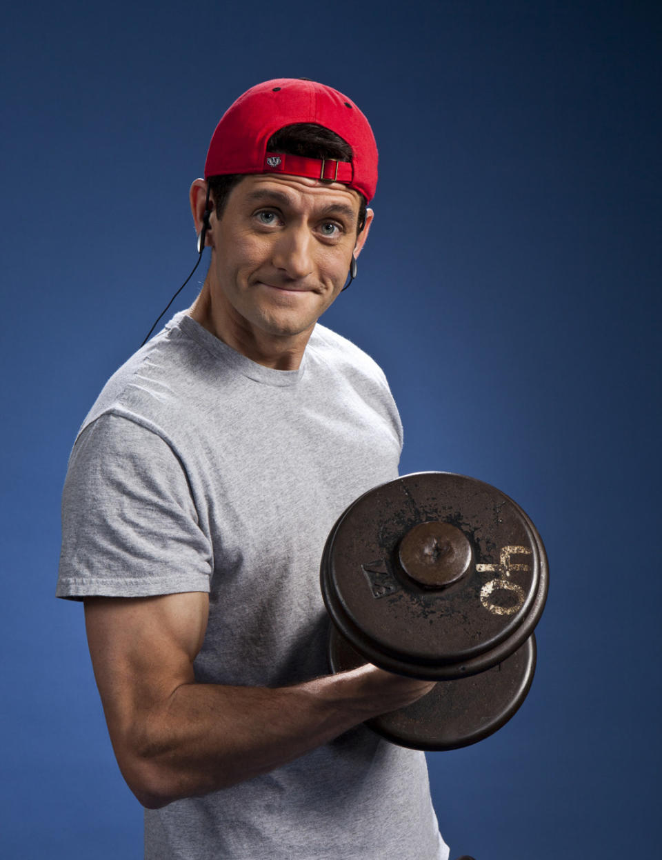 Paul Ryan wearing a backward baseball cap looking into the camera while lifting a weight with his right arm