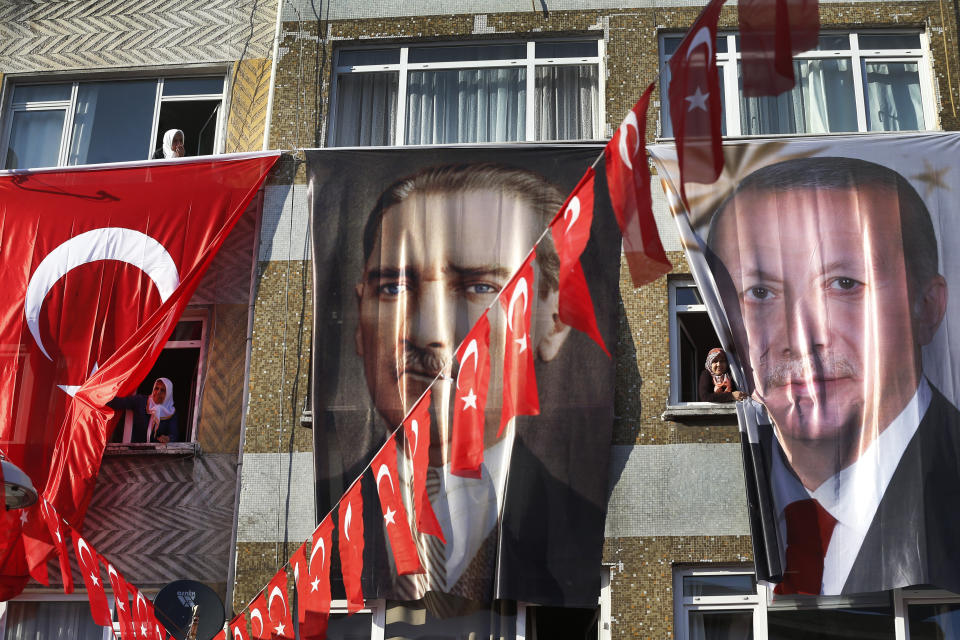 FILE-In this Tuesday, March 5, 2019 file photo, people peer out of their windows behind banners of Turkish Republic founder Mustafa Kemal Ataturk, centre and Turkey's current President Recep Tayyip Erdogan, right, following Erdogan speech at a rally in Istanbul, ahead of local elections scheduled for March 31, 2019. For Turkish President Recep Tayyip Erdogan, Sunday’s local elections are about Turkey’s future national “survival.” After 17 years in office, the Turkish leader has a tight grip on power, but he is campaigning hard for the strong mandate that he says he needs to protect Turkey against threats from domestic and foreign enemies. Analysts say the rhetoric is aimed at diverting attention away from rising inflation, a sharp increase in food prices and high unemployment. (AP Photo/Lefteris Pitarakis, File)