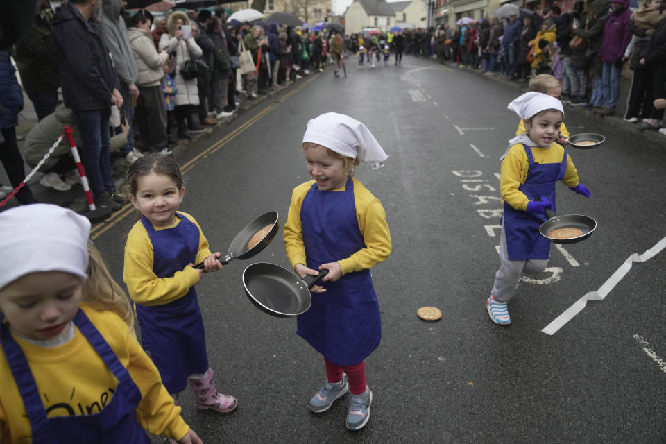Schoolchildren from local schools take part in the children's races prior to the annual Pancake race in the town of Olney, in Buckinghamshire, England, Tuesday, Feb. 13, 2024. Every year women clad in aprons and head scarves from Olney and the city of Liberal, in Kansas, USA, run their respective legs of the race with pancakes in their pans. According to legend, the Olney race started in 1445 when a harried housewife arrived at church on Shrove Tuesday still clutching her frying pan with a pancake in it. (AP Photo/Kin Cheung)
