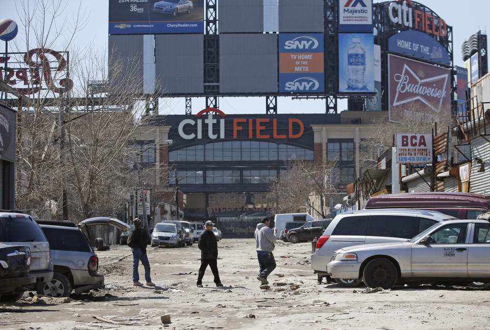 FILE - In this April 2, 2015 photo, workers cross an unpaved street adjacent to Citi Field, home to the New York Mets baseball team in the Willets Point section of the Queens borough of New York. New York City officials approved a plan Thursday, April 11, 2024, to build a 25,000-seat stadium for Major League Soccer’s New York City Football Club next to the New York Mets’ stadium, Citi Field. The $780 million soccer stadium, expected to open in 2027, will anchor a 23-acre redevelopment project in the neighborhood known as Willets Point that will also include housing, a new public school, retail stores and a hotel. (AP Photo/Kathy Willens, File)