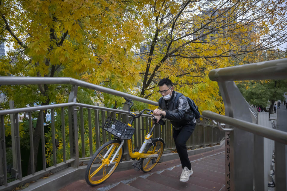 A commuter wearing a face mask pushes a bicycle across a pedestrian bridge in the central business district in Beijing, Friday, Oct. 28, 2022. (AP Photo/Mark Schiefelbein)