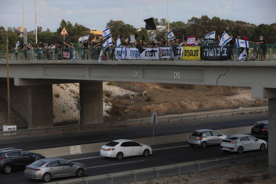 Israeli protesters hold flags and signs as they stand on a bridge to demonstrate against Israel's Prime Minister Benjamin Netanyahu near Beit Yanai, Israel, Saturday, Aug. 8, 2020. (AP Photo/Sebastian Scheiner)