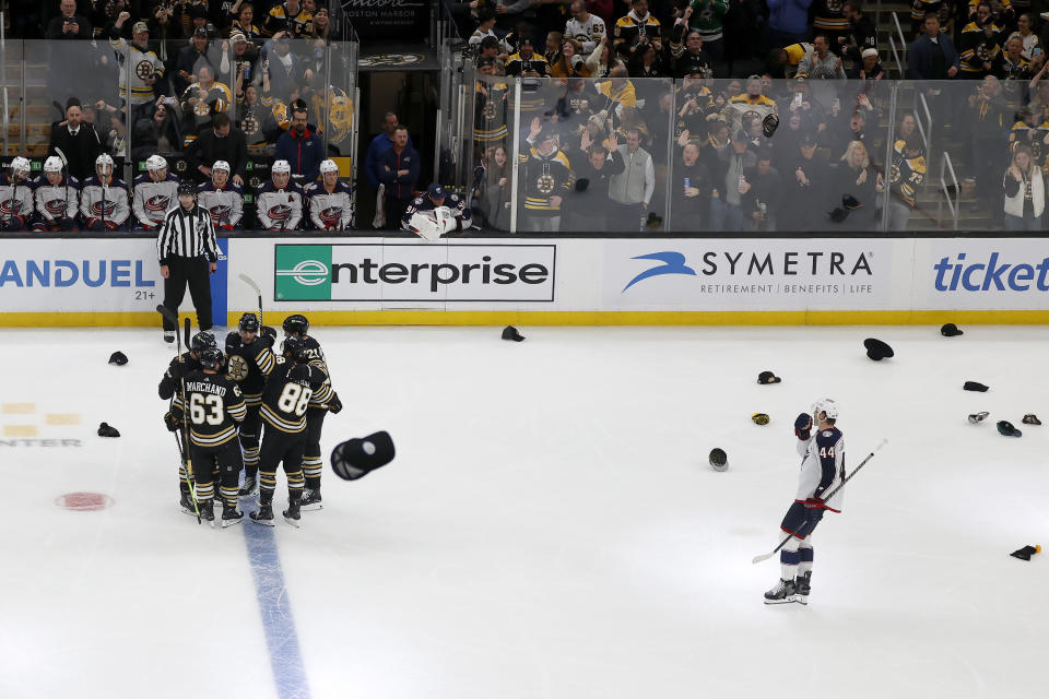 Hats fly onto the ice as Boston Bruins players congratulate teammate Brad Marchand (63) for scoring his third goal for a hat trick as Columbus Blue Jackets defenseman Erik Gudbranson (44) looks on during the third period of an NHL hockey game, Sunday, Dec. 3, 2023, in Boston. (AP Photo/Mary Schwalm)