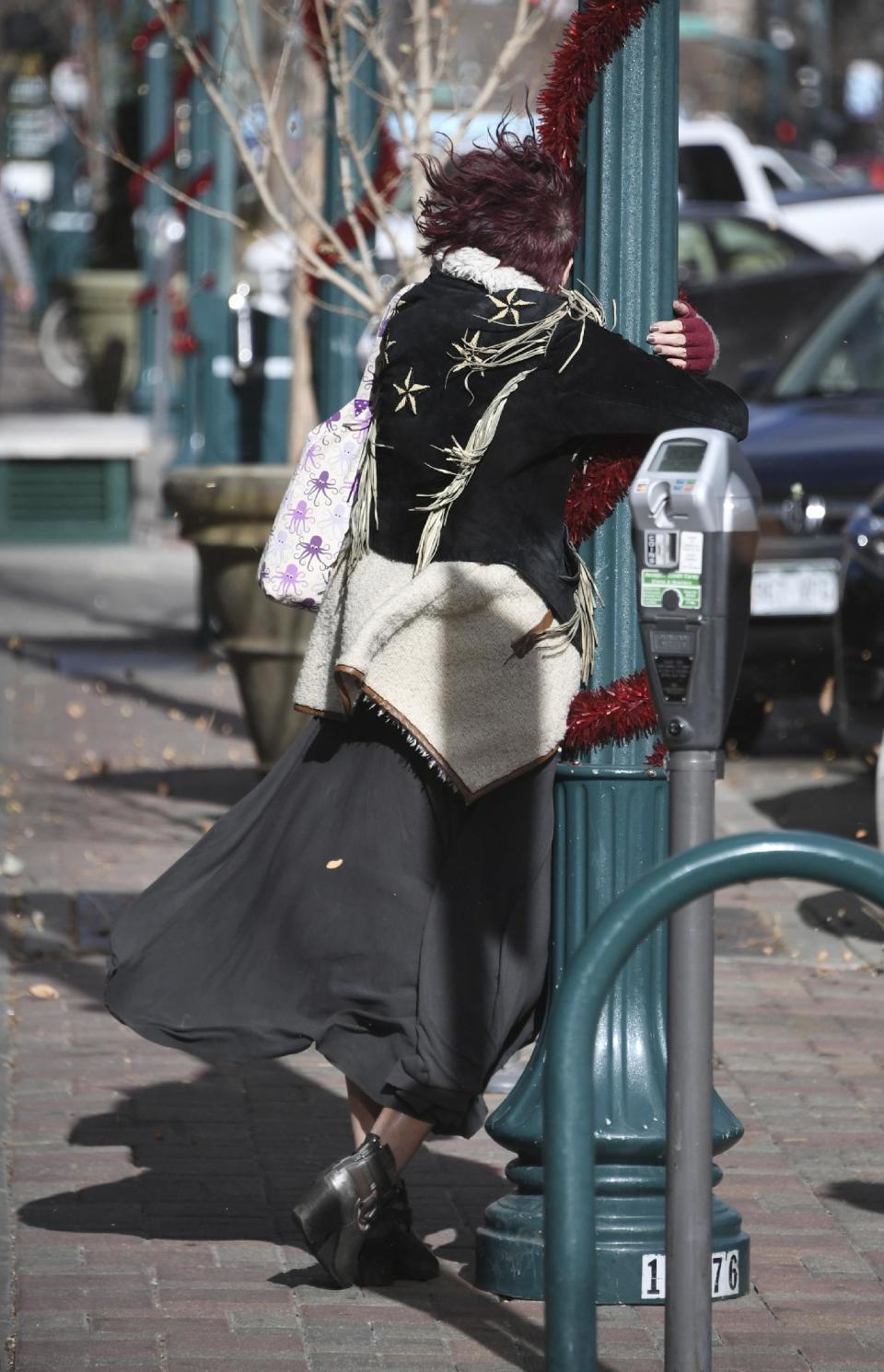 Marcia Curtis holds on tightly to a lamp post as she make her way to the downtown bus station in Colorado Springs, Colo. Friday, Dec. 16, 2016. (Mark Reis/The Gazette via AP)