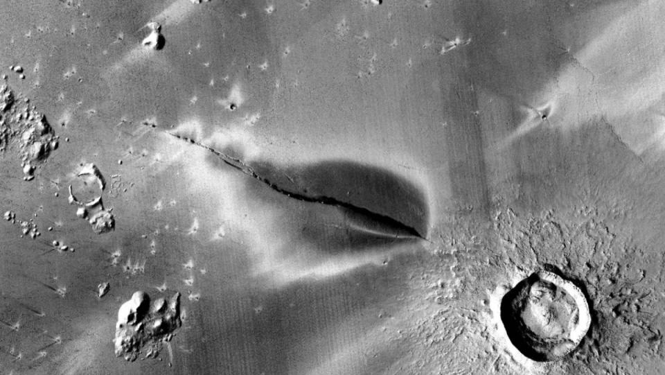 a photo of the surface of Mars with a dark shadow of a volcano