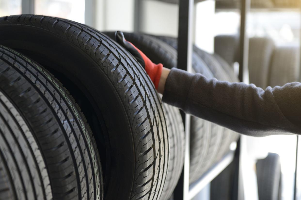 Male mechanic holding tire while repairing service garage background.