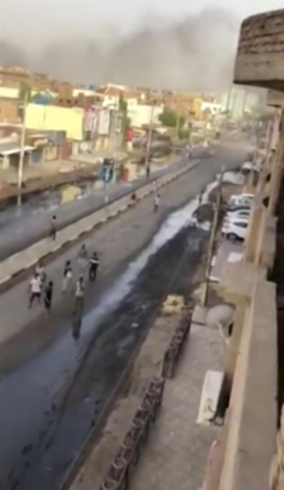 In this image made from video, civilians walk down a street in Khartoum, Sudan with plumes of smoke rising in the horizon on Monday, June 3, 2019. Sudanese security forces moved against a protest sit-in camp in the capital Monday, witnesses and protest organizers said. Machine gun fire and explosions were heard and smoke rose from the area. Protest organizers said at least two people were killed.(Elmontasir Darwish via AP)