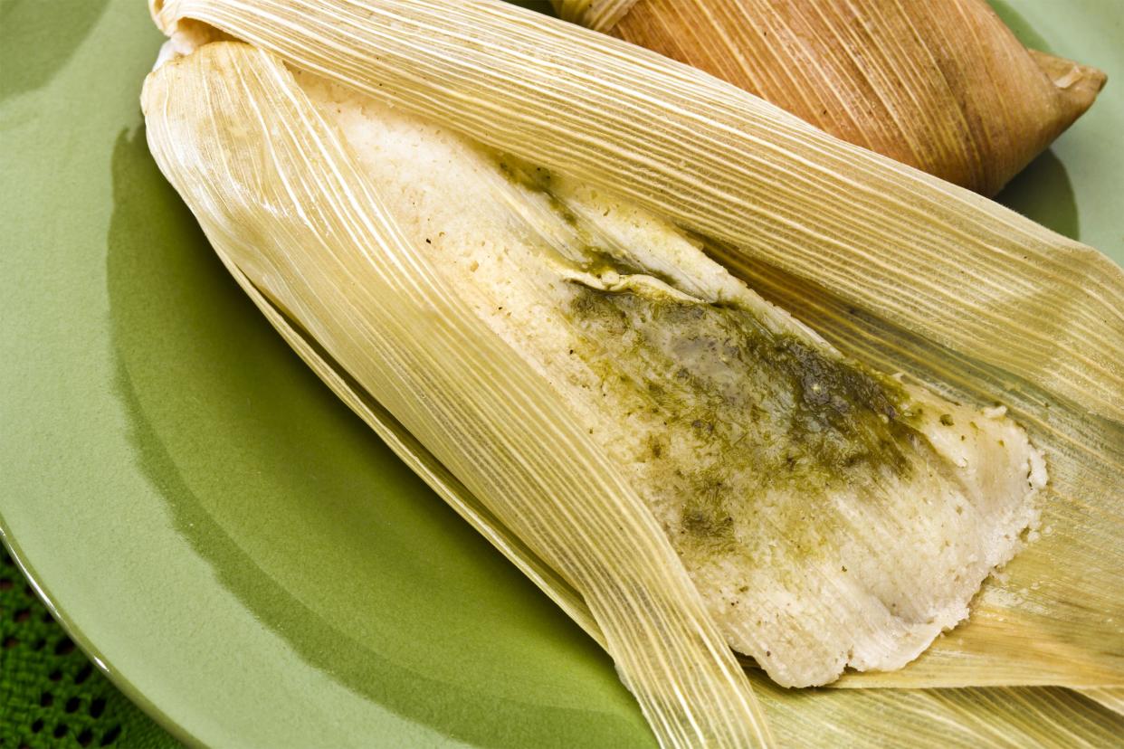 Two green chile chicken tamales, one is opened on an avocado green plate