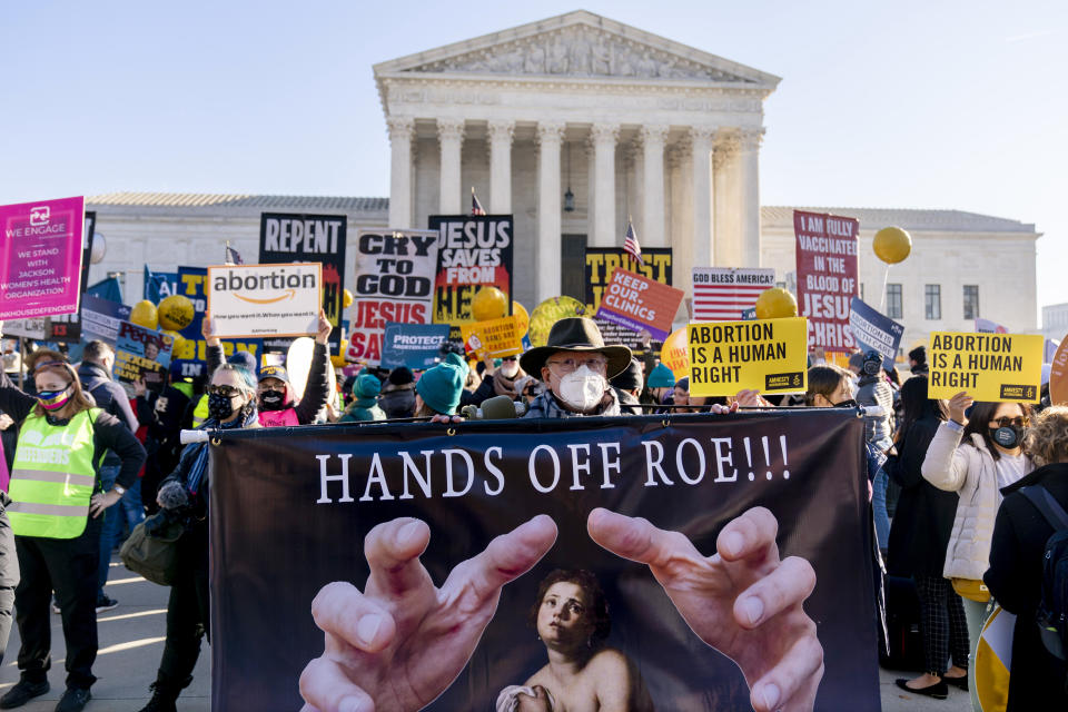 Demonstrators carrying signs gather outside the Supreme Court building. The most prominent sign reads 