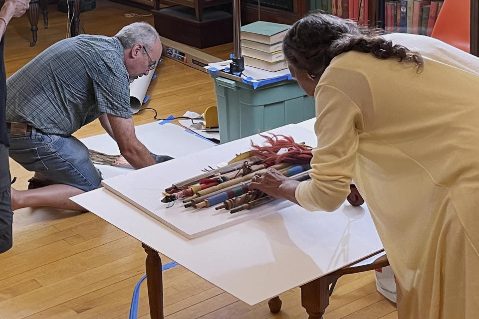 Leola One Feather, right, of the Oglala Sioux Tribe in South Dakota, lines up a grouping as John Willis photographs, left, Native American artifacts on July 19, 2022, at the Founders Museum in Barre, Massachusetts. The private museum, which is housed in the town library, is working to repatriate as many as 200 items believed to have been taken from Native Americans massacred by U.S. soldiers at Wounded Knee Creek in 1890. Willis is photographing the items for documentation, ahead of their expected return to the tribe. (AP Photo/Philip Marcelo)