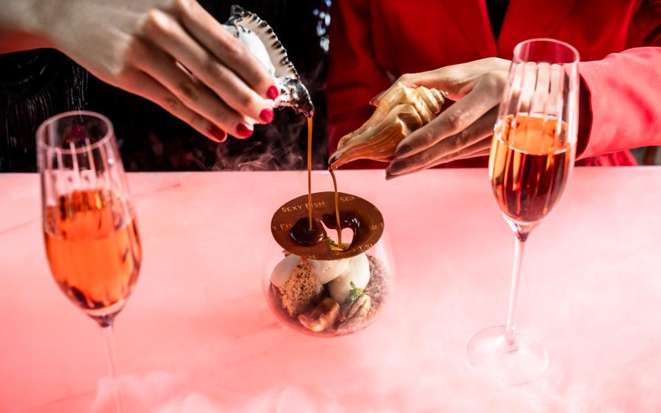 The top of the chocolate dessert melts as a waiter pours hot caramel on to it