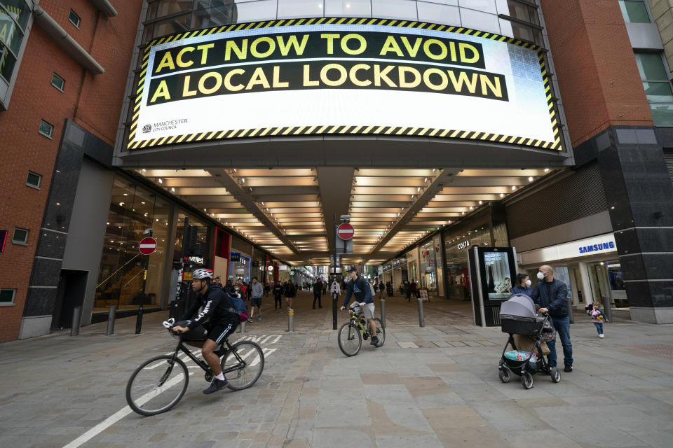 FILE - In this Tuesday Sept. 22, 2020 file photo, members of the public are seen by a public information message in Manchester, England. The British government is under pressure to develop a national strategy to combat the second wave of the COVID-19 pandemic and “rescue Christmas’’ as scientists warn the number of people hospitalized with the disease could almost triple by the end of next month unless something is done now. (AP Photo/Jon Super, file)