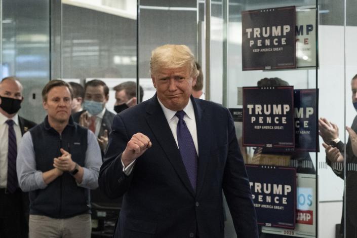 President Trump makes a fist with his right hand as he walks into a campaign office with Trump Pence signs