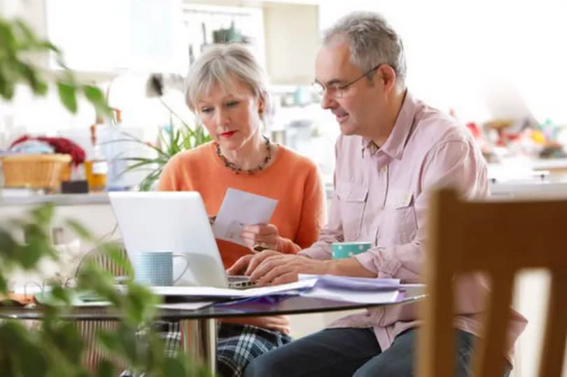 An older man and woman are sitting at a desk looking at a computer screen