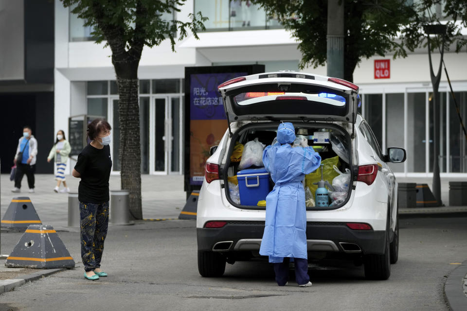 A woman wearing a face mask looks at a medical worker in protective gear preparing to collect coronavirus test samples at a closed shopping mall as part of COVID-19 controls in Beijing, Monday, June 13, 2022. China's capital has put school online in one of its major districts amid a new COVID-19 outbreak linked to a nightclub, while life has yet to return to normal in Shanghai despite the lifting of a more than two month-long lockdown. (AP Photo/Andy Wong)