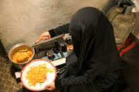 Amal Hasan scoops rice and potato from a pot to a plate to feed her children at their hut in Sanaa