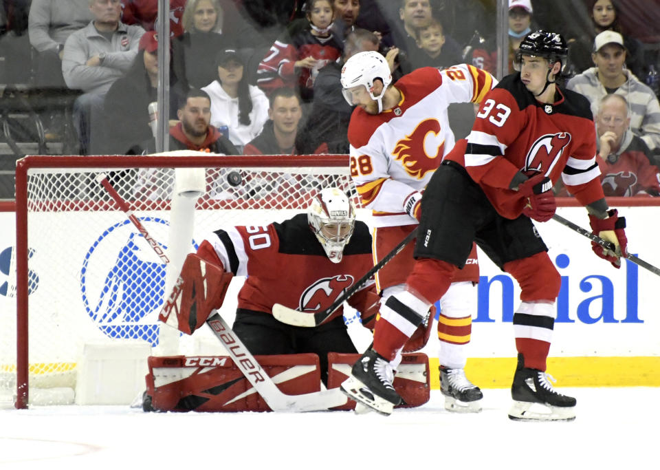 Calgary Flames center Elias Lindholm (28) tips the puck into the net for a goal past New Jersey Devils goaltender Nico Daws (50) as Devils defenseman Ryan Graves (33) looks on during the first period of an NHL hockey game Tuesday, Oct. 26, 2021, in Newark, N.J. (AP Photo/Bill Kostroun)