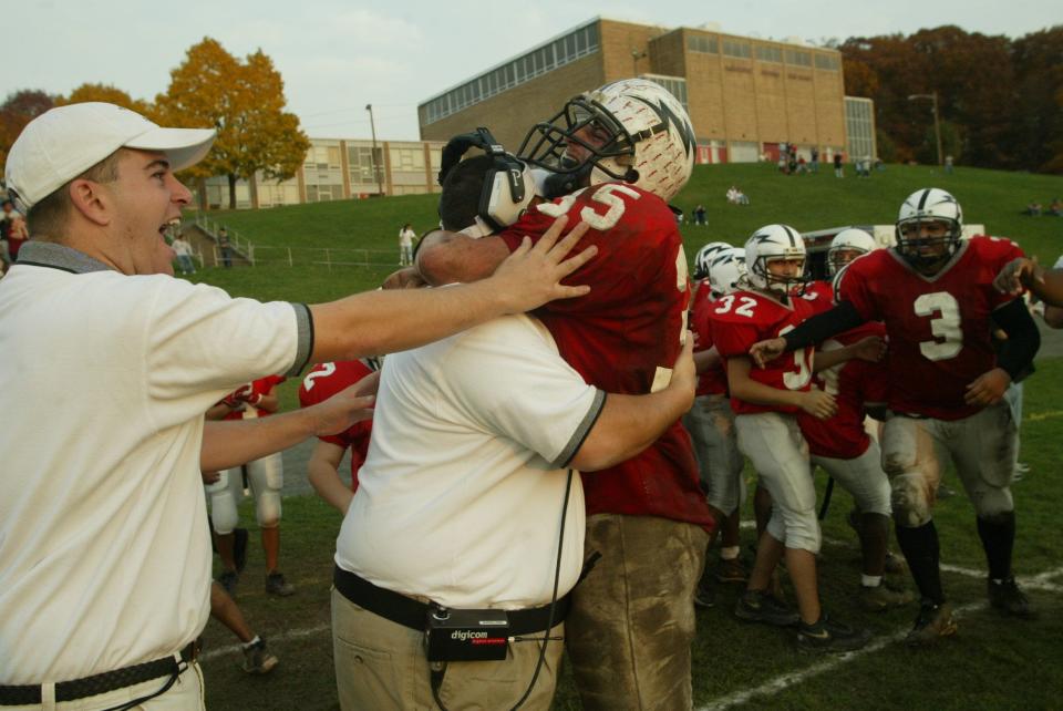 Nov. 1, 2003 (Haledon) -- Manchester Regional High School's Burim Ala, #35 bear hugs head coach Rande Roca after Manchester scored a touchdown putting them ahead of Midland Park, 43-32. Offensive line coach Jon Banta, far left, joins the festivities on the sideline. Manchester clinched a playoff appearance with their victory. Photo by Amy Newman/Herald News