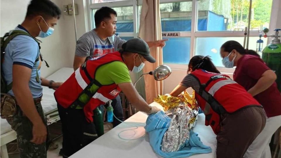 Ang mga manggagawa ng Philippine Red Cross ay naglalagay ng isang bata na nakabalot sa isang emergency blanket sa isang kama ng ospital