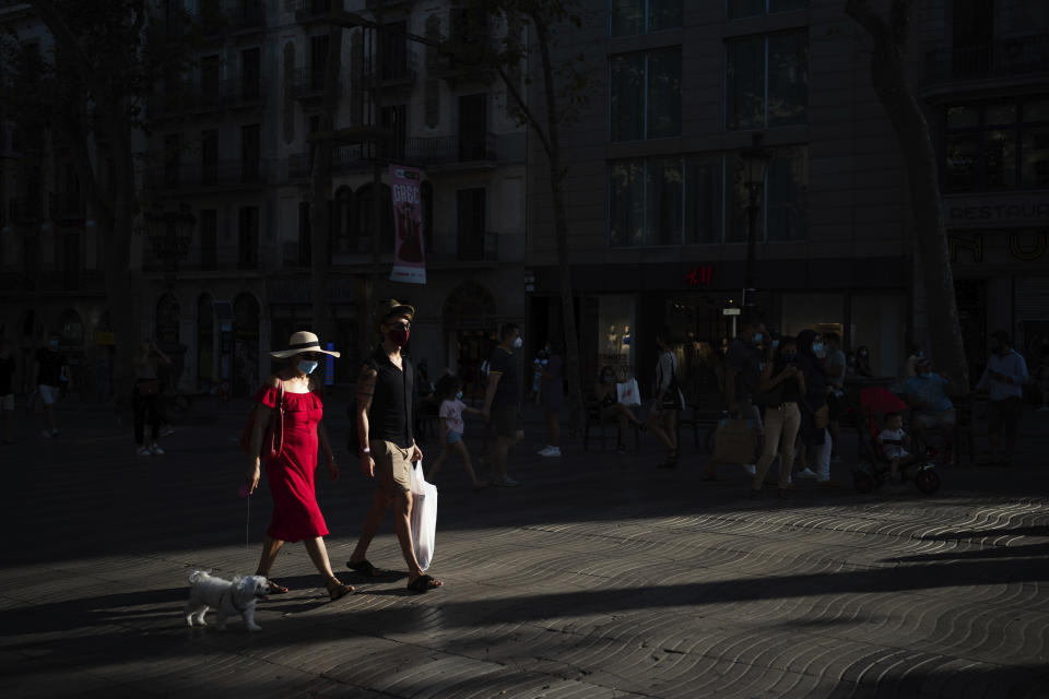 People wearing a face mask walk on Las Ramblas in Barcelona, Spain, Monday, July 27, 2020. Britain has put Spain back on its unsafe list and announced Saturday that travelers arriving in the U.K. from Spain must now quarantine for 14 days. (AP Photo/Felipe Dana)