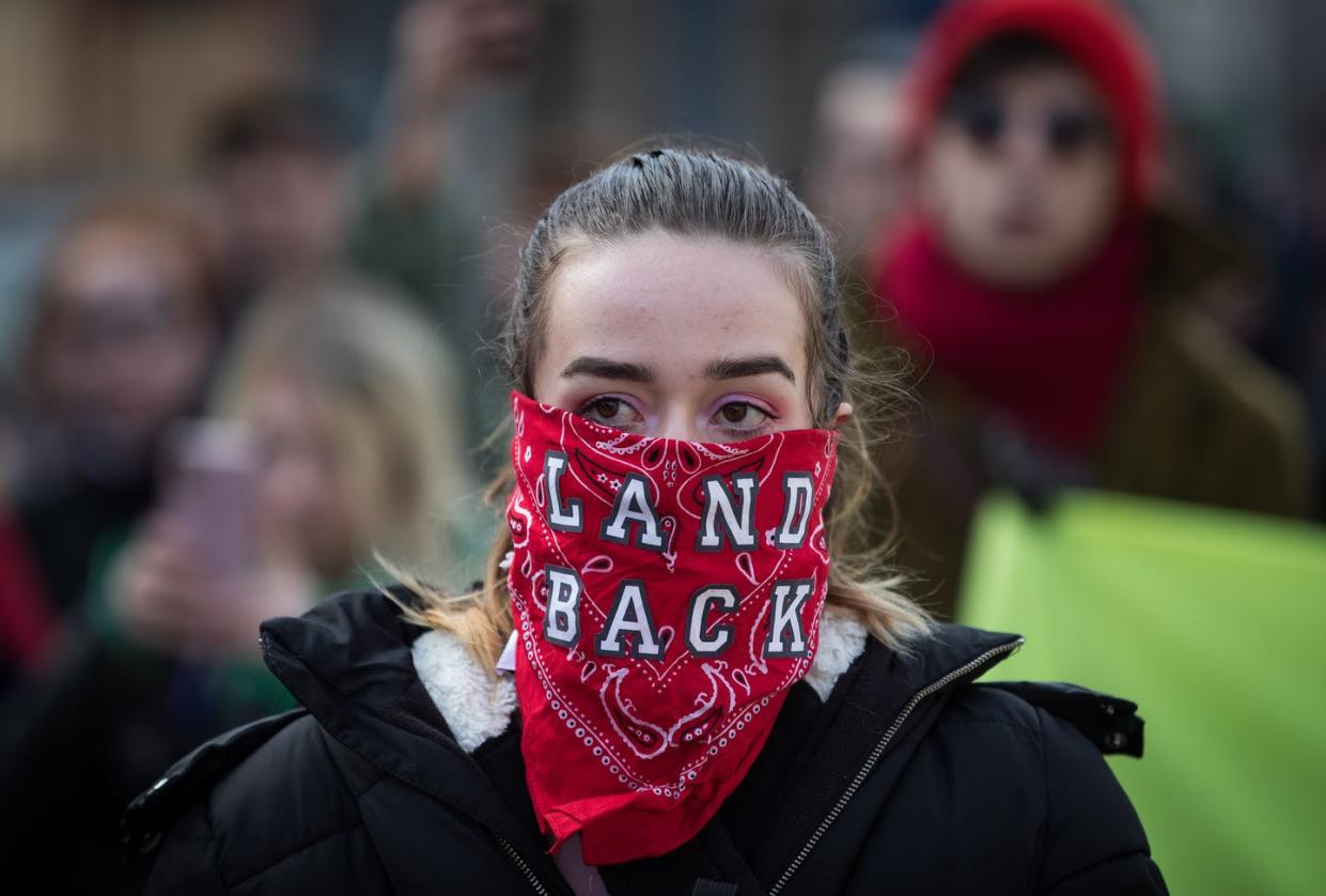 <span class="caption">A woman wears a bandana over her face reading 'Land Back', as people march to block a road used to access to the Port of Vancouver, during a demonstration in support of Wet'suwet'en Nation hereditary chiefs in February 2020. </span> <span class="attribution"><span class="source">THE CANADIAN PRESS/Darryl Dyck</span></span>