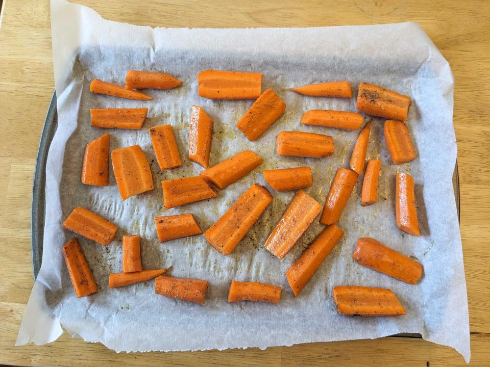 A baking sheet lined with parchment paper with several pieces of carrots covered in seasonings arranged on it