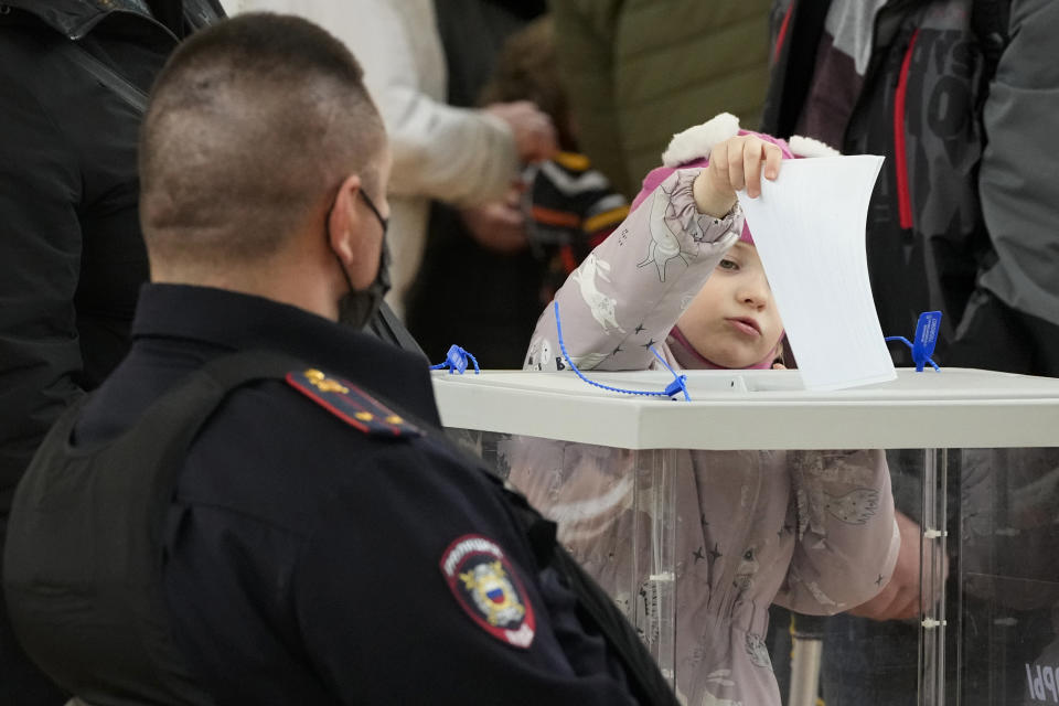 A child casts his parent's ballot as a police officer guards at a polling station during the presidential election in St. Petersburg, Russia, Sunday, March 17, 2024. Voters in Russia are going to the polls for the last day of a presidential election that is all but certain to extend President Vladimir Putin's rule after he clamped down on dissent. (AP Photo/Dmitri Lovetsky)