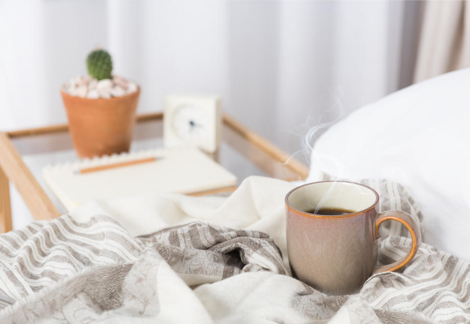 Cup of coffee on cozy white bed with cactus flowerpot,memo pat and alarm clock on wood bed side table