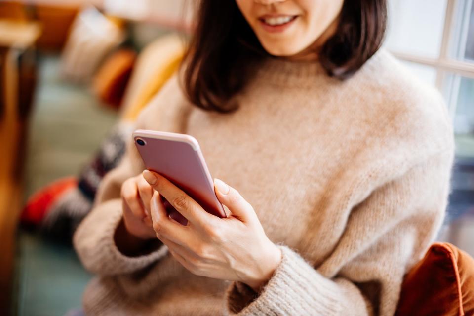 Woman wearing turtleneck sweater looking at pink smartphone