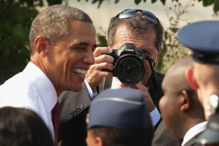 Man smiling and looking into a camera lens held by a photographer surrounded by people