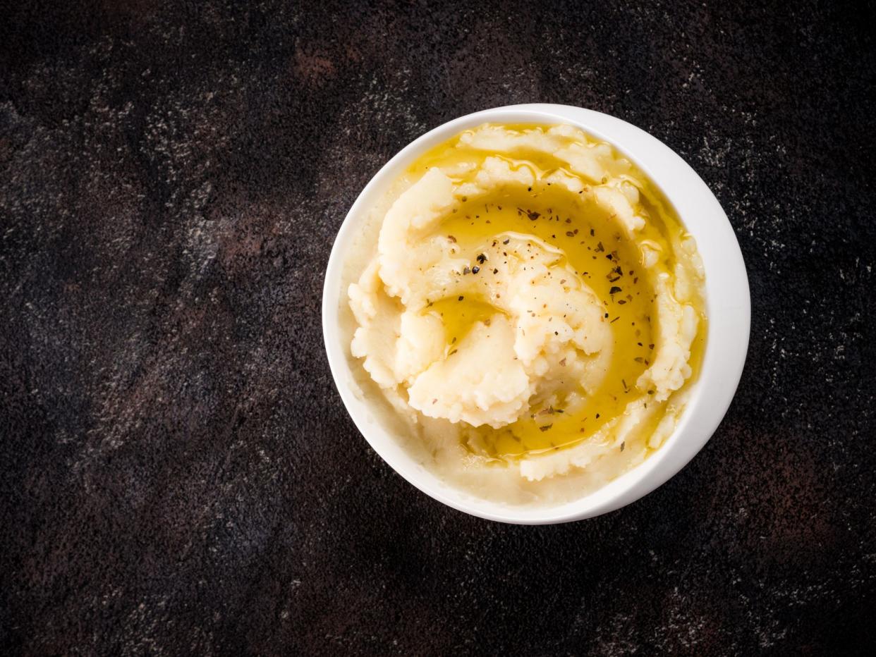 Mashed potatoes with spices and olive oil in white bowl on dark concrete background. Top view or flat lay. Copy space.