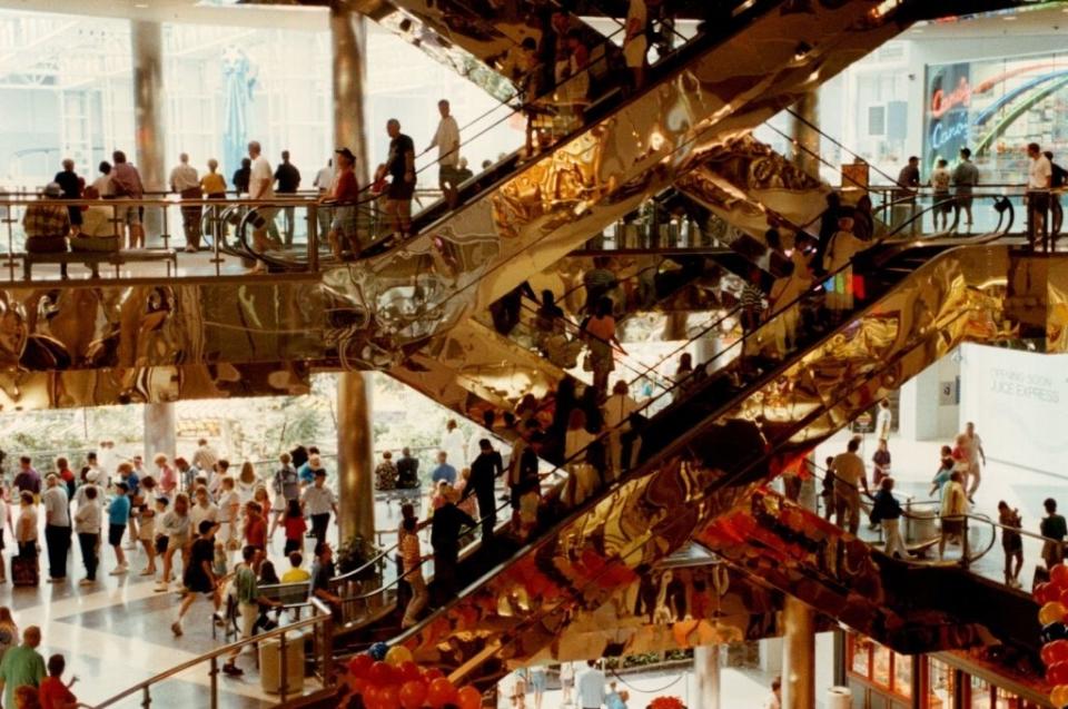 People milling around a busy multilevel shopping center with escalators and decorative elements