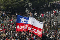 Anti-government demonstrators protest below a Chilean flag with the words "Chile Woke Up" in Spanish, during a protest in Santiago, Chile, Tuesday, Oct. 22, 2019. Chile has been facing days of unrest, triggered by a relatively minor increase in subway fares. The protests have shaken a nation noted for economic stability over the past decades, which has seen steadily declining poverty despite persistent high rates of inequality. (AP Photo/Esteban Felix)