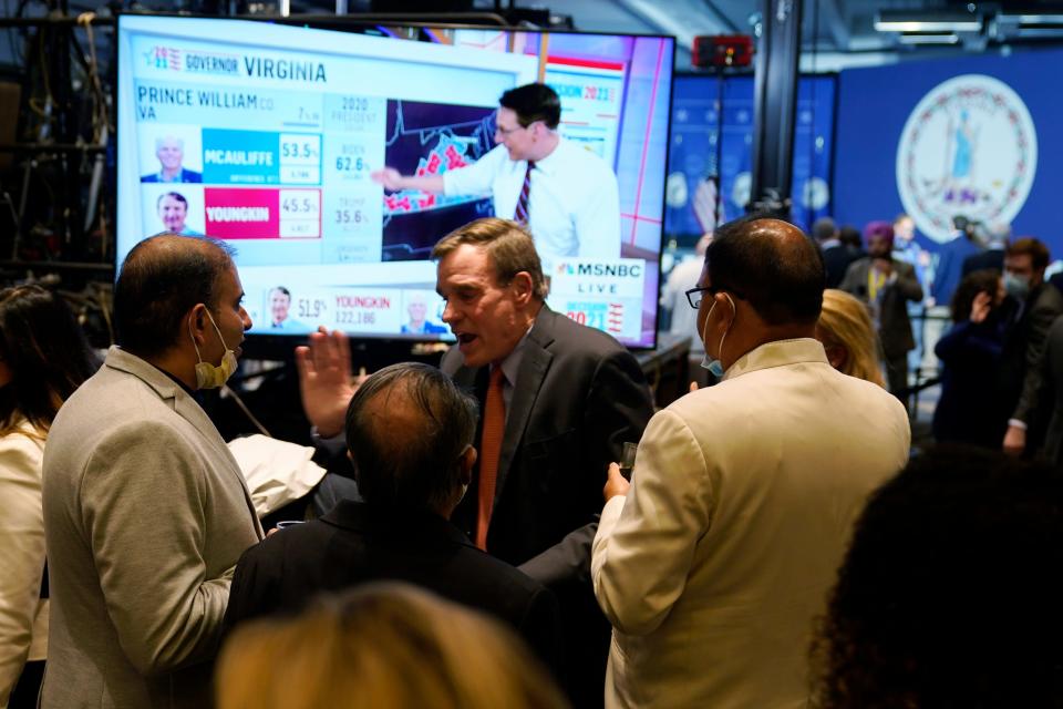 Sen. Mark Warner, D-Va., walks past a screen displaying early vote totals at an election party in McLean, Va., on Tuesday. Voters are deciding between Democrat Terry McAuliffe and Republican Glenn Youngkin.