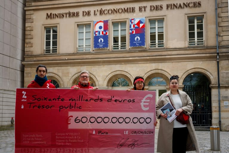 Des militants d'Attac tiennent un "chèque" géant de 60 milliards d'euros, ce facsimilé représentant, selon eux, le déficit public qui pourrait être comblé en taxant les très riches plutôt qu'en taillant dans les dépenses, devant le ministère de l'Economie et des Finances, le 8 avril 2024 (Dimitar DILKOFF)