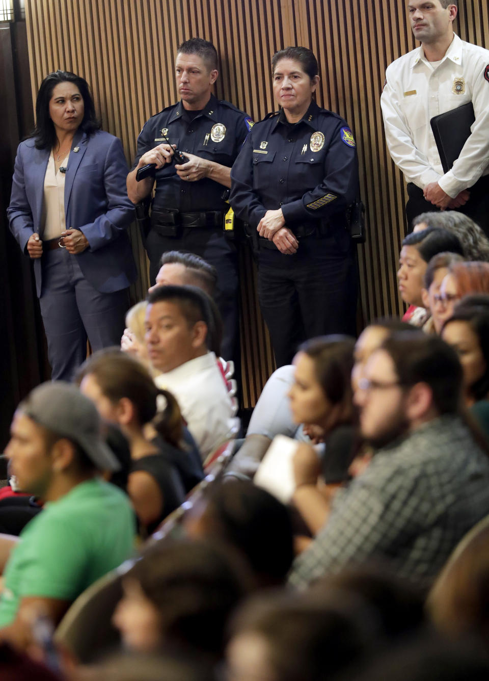 Phoenix police officers stand along the wall as protesters angered by a video of Phoenix officers who pointed guns and yelled obscenities at a black family they suspected of shoplifting gather inside City Council chambers, Wednesday, June 19, 2019, in Phoenix to demand reforms. Speakers called on the council to fire the officers involved in the videotaped incident and to create a board of civilians to oversee changes in department procedures. (AP Photo/Matt York)